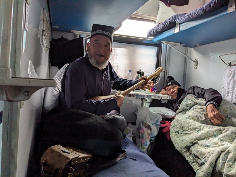 A grandpa playing a two-string guitar in his bed