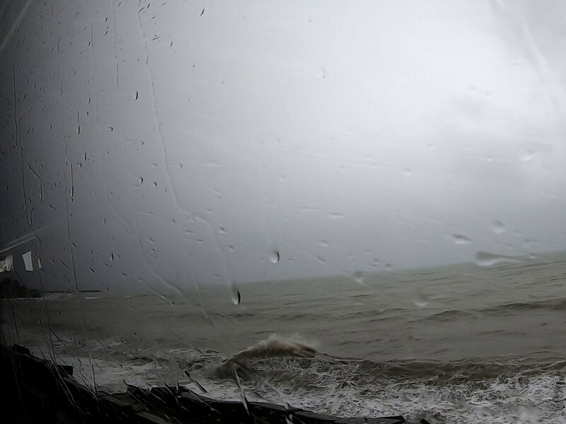 Waves breaking on the shore, seen through a wet bus window